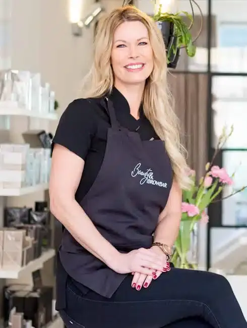 Wendy zit lachend in de salon, met het schort van Beauty & Browbar voor.